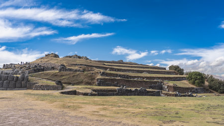 Ruins of the ancient Inca fortress Sacsayhuaman. Terraces on the hill, walls of polygonal ashlar masonry. Green grass on the field. Blue sky, clouds. Peru. Cuscoの写真素材