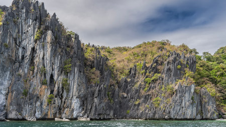 Picturesque coastal karst cliffs surround the bay. Steep, furrowed slopes, sharp peaks, and green vegetation. Blue sky, clouds. Philippines. Palawan. Cadlao Lagoon. Bacuit bayの写真素材