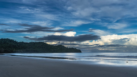 Early morning by the ocean. The waves are spreading across the sandy beach, without people. A hill...