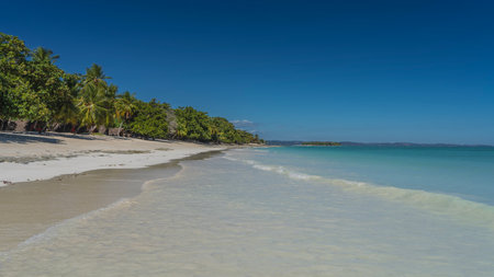 A beautiful tropical beach without people. The waves of the aquamarine ocean spread over the white...