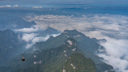 Beautiful mountain landscape. Green vegetation on the slopes. Peaks above the clouds. Cable car cabin on the background of the sky. China. Tianmen Mountainの写真素材