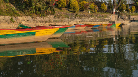 Bright colorful wooden tourist boats are moored in a row near the shore. Reflection on the calm, shiny water. Nepal. Phewa Lake. Pokharaの写真素材