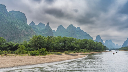 Beautiful calm river. Tourist ships and bamboo rafts float along the riverbed. There is green vegetation on the sandy shores. Picturesque mountains against the sky and clouds.の写真素材