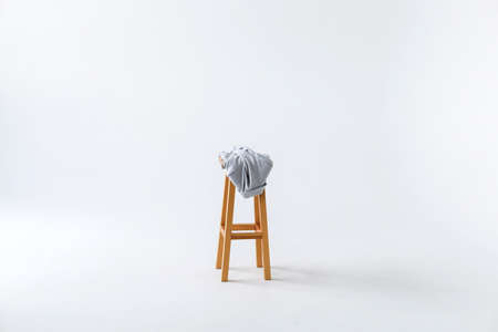 A brown wooden, backless high chair with a light gray jacket rests in the center of the room against a white isolated backgroundの写真素材