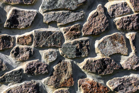 Stone brown background of different shapes with smeared cement around stones, bright sunlightの写真素材