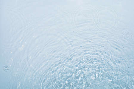 Blue water background with round streaks of drops dripping and creating vibrations, top view