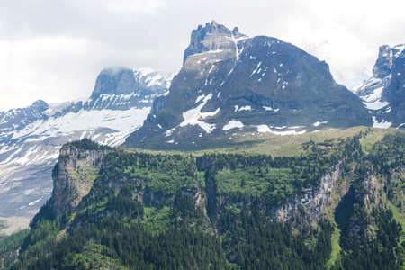Beautiful landscape of the Swiss cloud top of snow-capped mountains with green meadows and trees on...