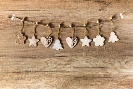 Christmas garland of wooden figurines of trees, stars, flowers and hearts on a wooden brown background. Christmas, winter, new year holiday concept. Flat lay, top view, copy spaceの写真素材