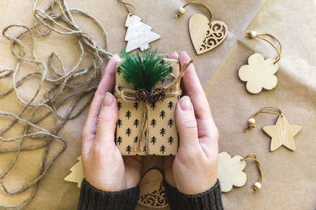 A girl in a dark sweater holds a gift box with a green spruce twig and cones, around a brown...