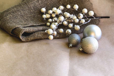 On a brown background lies a rough linen cloth with a branch in white berries and three shiny silver Christmas balls. space for textの写真素材