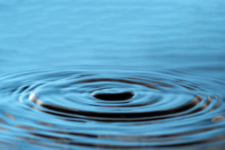 On the surface of the blue water, wavy circles spread in different directions. Place for advertisement and textの写真素材