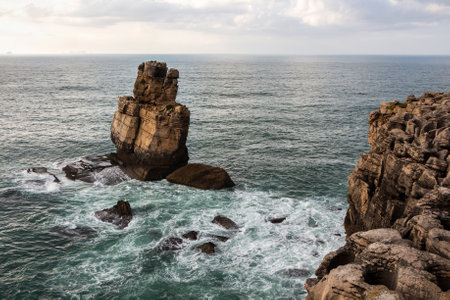 Landscape of the Atlantic Ocean with one isolated rock formation and a high rocky shore washed by turquoise water. Portugal, Peniche.の写真素材