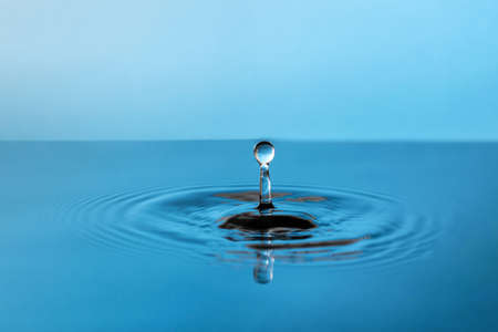 A high splash of a blue drop of water, on the surface of vibration in the form of blurring circles. Great idea for designの写真素材