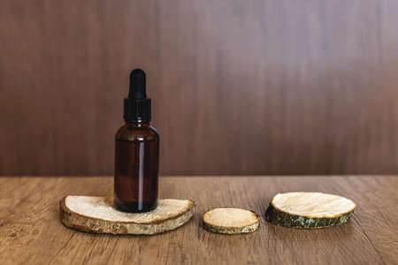 A brown, glass serum bottle with a pipette on a natural wood podium, next to empty podiums on a textured table. Idea for advertisingの写真素材