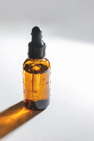 Moisturizing serum in a glass translucent bottle in water droplets with a dark dropper on a white...
