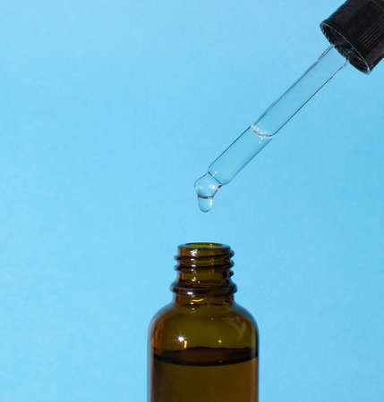 The serum drips from a pipette on the side into a glass brown bottle on a blue background, copy spaceの写真素材