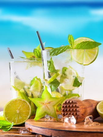Summer lime cocktail , drink with fresh fruits on wooden table and tropical beach  Blue sky, seaの写真素材
