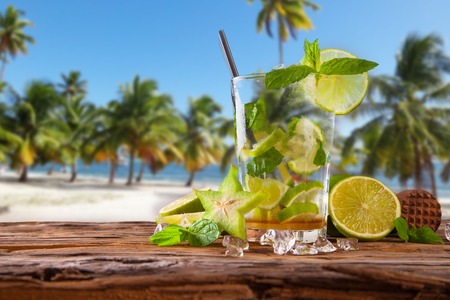 Summer lime cocktail , drink with fresh fruits on wooden table and tropical beach  Blue sky, seaの写真素材