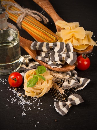 Pasta spaghetti, vegetables and spices, on wooden table, on balck stone backgroundの写真素材