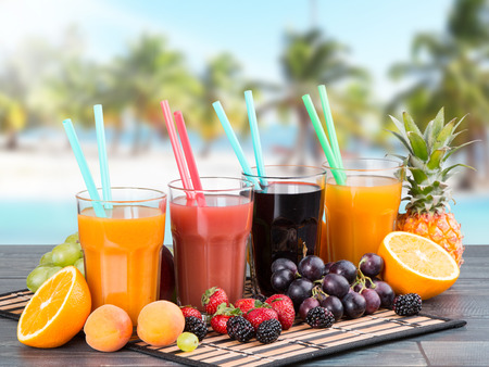 Orange, stawberry and blackberry juice on wooden table with tropical beach backgroundの写真素材