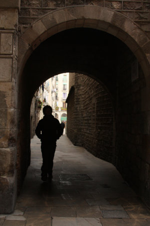 A silhouette of a person walking through an old stone archway in a historic European alley. The contrast between shadow and light, mysterious and cinematic atmosphereの写真素材