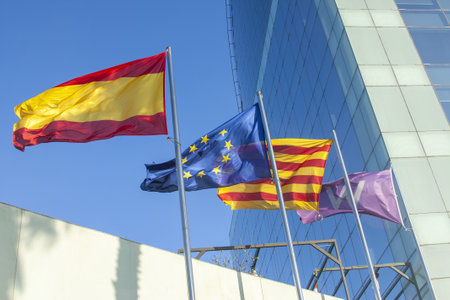 A set of flags waving in the wind against the backdrop of a modern glass building and a clear blue sky.の写真素材