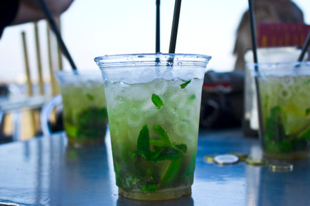Close-up of a mojito with ice and mint leaves in a clear cup. Detail-oriented, casual setting, and...