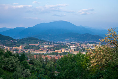Scenic landscape with a town, hills, and mountains. Green trees and evening sky.