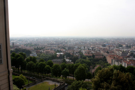 Hazy, elevated view of Bergamo, Italy, with red-tiled roofs and green spaces. Distant Alps and overcast skyの写真素材