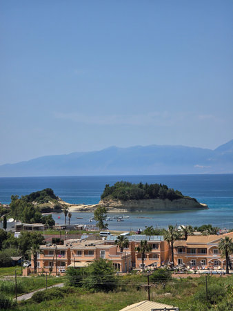 A scenic view of a Greek island resort, with the blue Ionian Sea and distant hazy mountains.