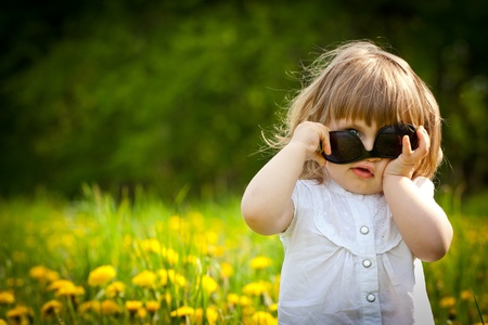 Little girl in a dandelion meadow puting sunglasses upside downの写真素材