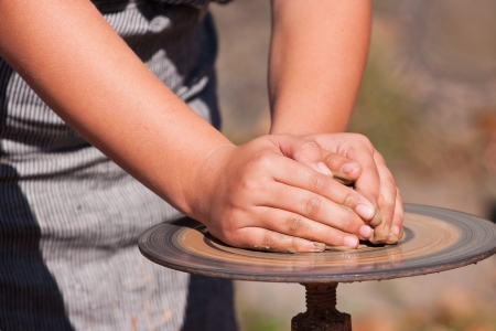 Child hands on a potter wheel forming wet clayの写真素材