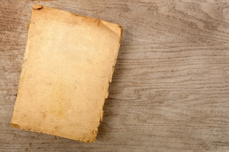 Old closed softcover book with yellowed pages on a wooden backgroundの写真素材