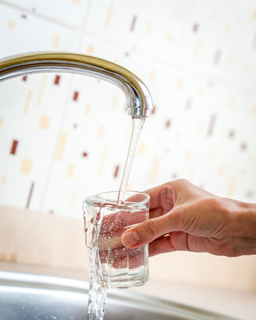 Water poured from tap to glass hold by handの写真素材