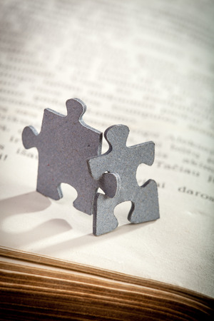 Concept of friendship and learning: closeup of two jigsaw puzzle pieces on a page of  book. Shallow depth of fieldの写真素材