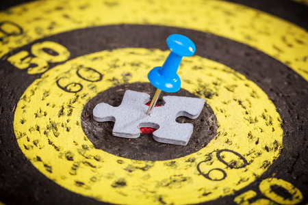 Targeting customers concept: blue pin stuck to a man shape jigsaw puzzle piece on old target boardの写真素材
