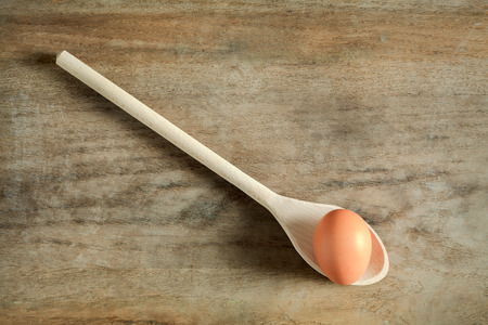 Raw brown hen egg on wooden spoon on old vintage cutting board. View from aboveの写真素材