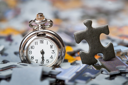 Pocket watch on a pile of jigsaw puzzle pieces by separated black jigzaw piece. Shallow depth of fieldの写真素材