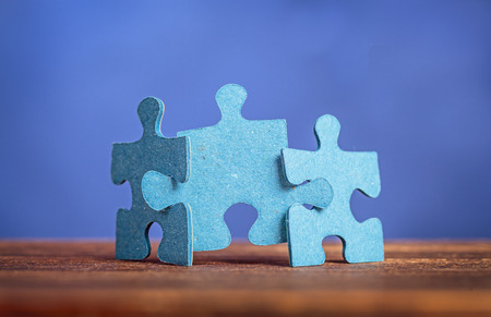 Three jigsaw puzzle pieces on a table joint together against blue background. Shallow depth of fieldの写真素材