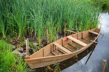 Brown wooden rowing boat on the lake by green high grassの写真素材