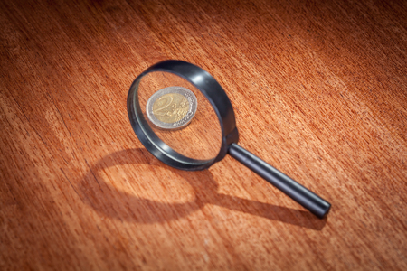 Magnifying glass and two euro coin on tableの写真素材