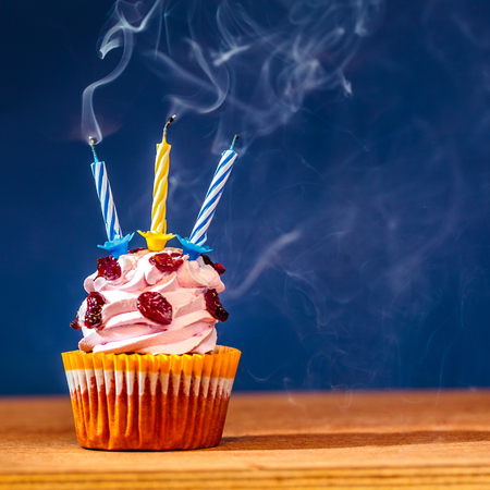 Cupcake with three blown out candles on top over deep blue background in a cloud of a smokeの写真素材