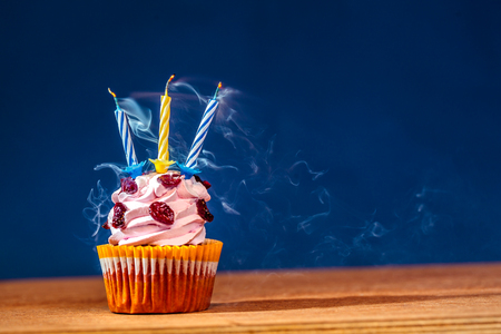 Birthday cake with three blown up candles in smoke over blue backgroundの写真素材