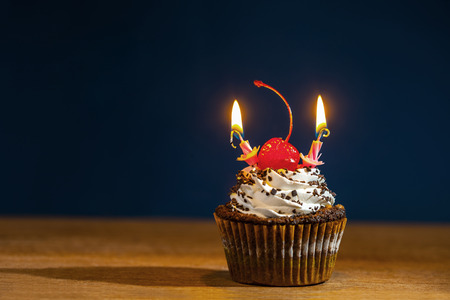 Cupcake with red cherry and two burning candles over dark backgroundの写真素材
