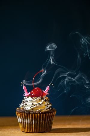 Birthday cupcake with red cherry and blown candles in cloud of smoke over dark backgroundの写真素材