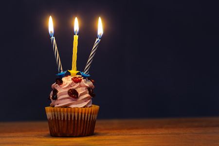 Birthday cake with three burning candles over dark blue backgroundの写真素材