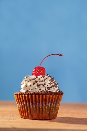 Fresh cupcake with red cherry on top over blue backgroundの写真素材