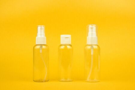 Empty cosmetic plastic bottles with pump and spray for shampoo and gel on yellow background. Clear...