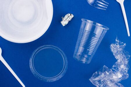 White plastic disposable tableware, utensil flat lay on trendy blue background. Contrast color. Plastic plate, bowl, spoon, fork. Top view copy space. Recycling concept. Template for web. Stock photo.の写真素材