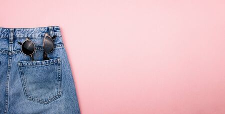 Sunglasses in jeans pocket flat lay on trendy pink background. Summer, holidays and vacation concept. Colorful summer fashion outfit top view. Banner template for web, advertising, media. Stock photo.の写真素材